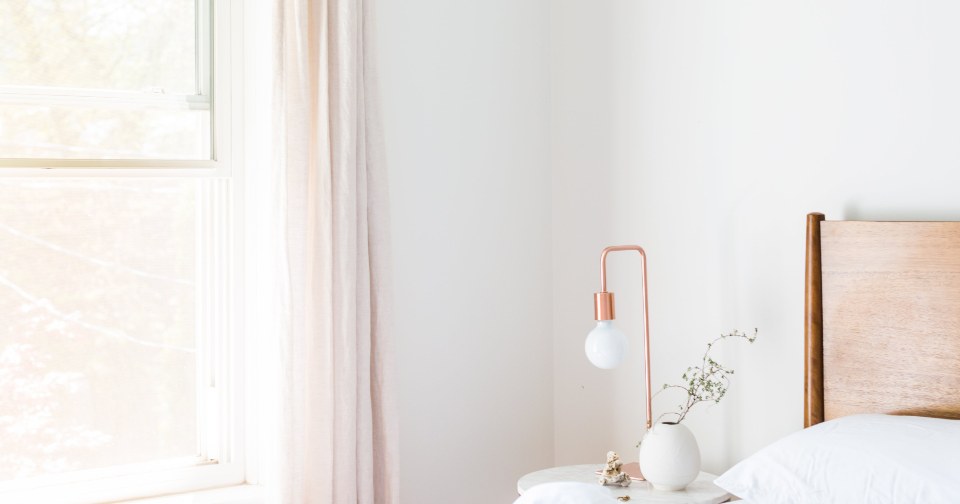 A bright, calm bedroom with a bedside lamp and white bedding