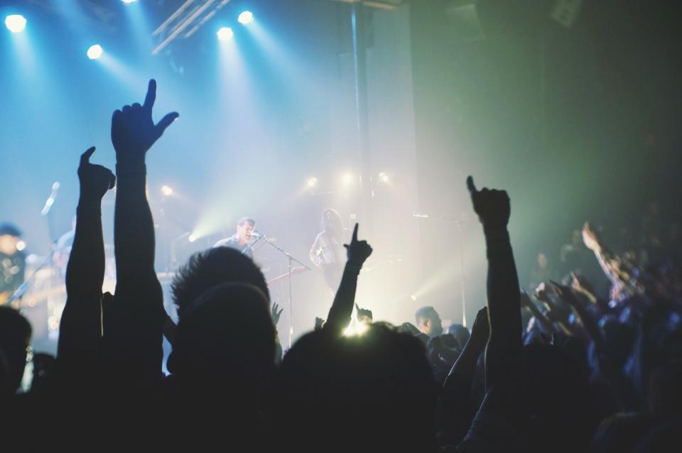 A concert crowd with raised hands under stage lights