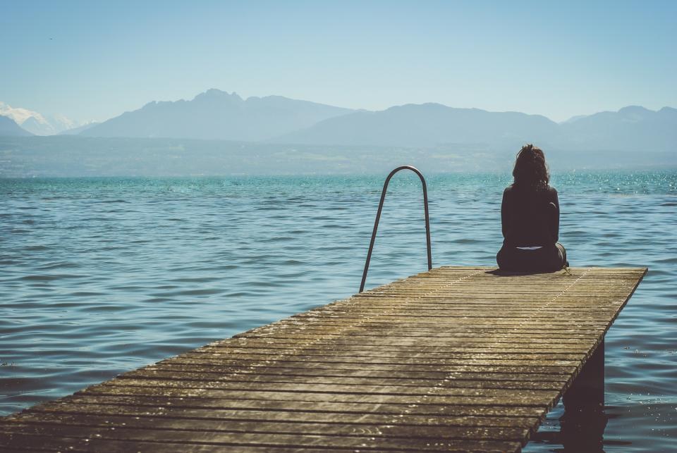 A person sitting on a wooden dock looking out over a calm lake