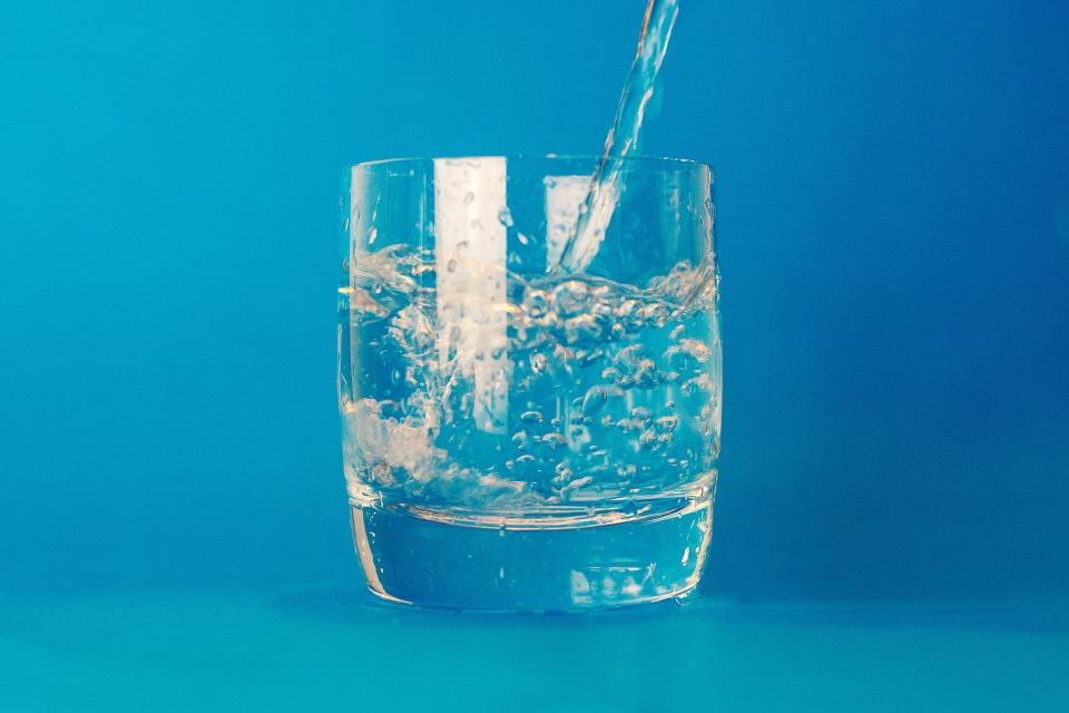A glass of water being filled against a blue background
